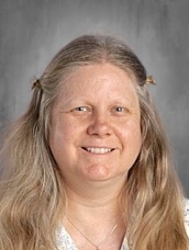 A smiling woman with long, wavy hair, wearing a light-colored top, against a neutral background.