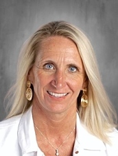 A smiling woman with long blonde hair, wearing earrings and a white jacket, against a neutral background.