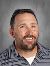 Smiling man with a beard, wearing a striped shirt, against a gray background.