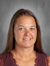 Headshot of a woman with long brown hair, wearing a maroon top, set against a gray background.