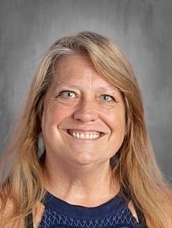 Smiling woman with long blonde hair, wearing a navy blue top, against a gray background.