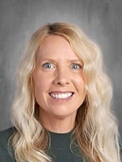 Smiling woman with long, wavy blonde hair, wearing a green top, against a neutral background.