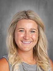 Smiling woman with long, wavy blonde hair, wearing a striped shirt, against a gray background.